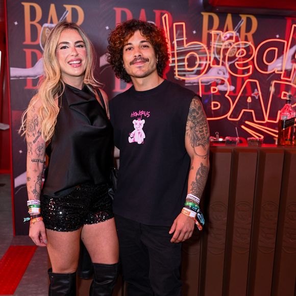 Douglas Sampaio e Camila Gentile: o ator aposta em uma regata machão preta com estampa gráfica de ursinho, calça jeans preta reta e tênis escuro de sola branca. Já sua companheira usa um top de cetim preto com gola degagê, shorts de paetês pretos, botas de cano alto over the knee e acabamento acetinado