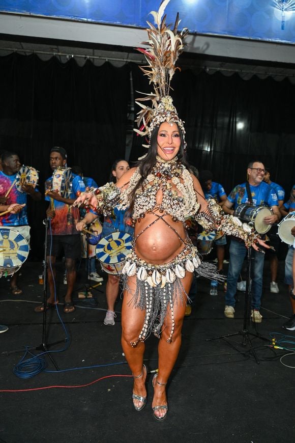 O look de Sabrina Sato para o ensaio da Vila Isabel combina búzios naturais, pedrarias reluzentes e miçangas em tons terrosos e perolados, valorizando a inspiração praiana da produção