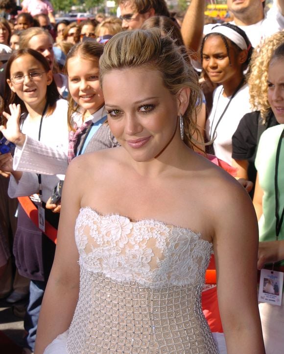 No tapete vermelho de 'A Nova Cinderela', em 2004, Hilary Duff exibia a pele jovem aos 16 anos; hoje, aos completos 39, a atriz mantém uma aparência natural e cuidada, valorizando a qualidade da pele