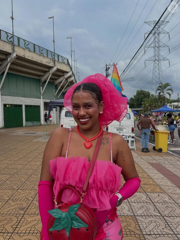Para mulheres de estilo arrojado, a bolsa de morango ganha ainda mais destaque quando combinada com peças em tons de rosa, criando uma produção feminina, vibrante e moderna