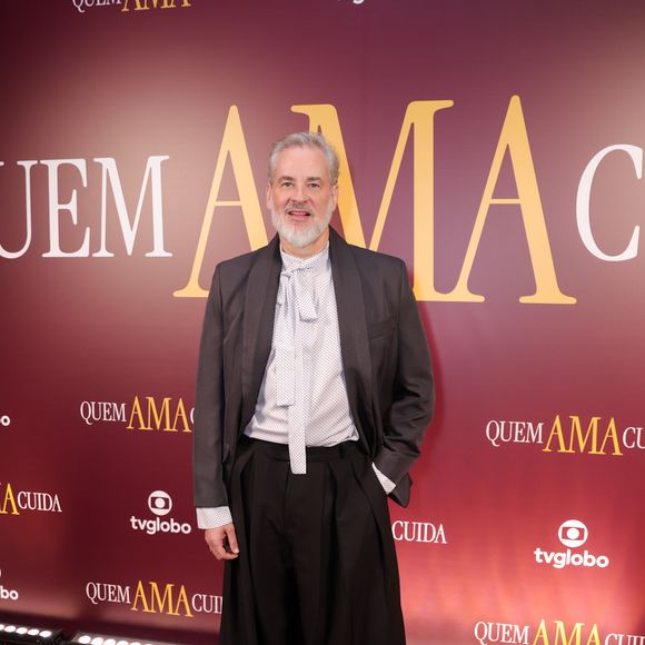 Dan Stulbach exibiu uma proposta de alfaiataria desconstruída e contemporânea. Ele combinou um blazer cinza grafite com uma camisa branca de padronagem delicada, cujo destaque é o laço frontal longo substituindo a gravata tradicional. Na parte inferior, uma calça pantaloona preta de cintura alta e modelagem extremamente ampla trouxe volume ao visual, finalizado com sapatos pretos de sola robusta
