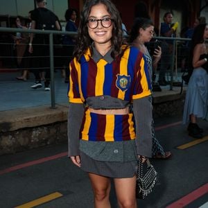 Samantha Alves desfilou uma estética preppy desconstruída e vibrante, utilizando um conjunto de tricô listrado em azul, amarelo e bordô, que remete a uniformes escolares clássicos com um toque subversivo. O look apresenta um corte cropped tanto na blusa quanto na sobreposição, revelando uma base de alfaiataria cinza risca-de-giz por baixo
