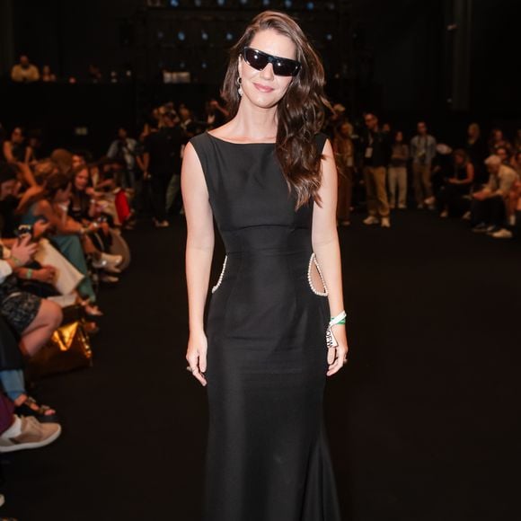 A atriz Nathalia Dill apostou no minimalismo sofisticado do 'pretinho nada básico', vestindo um longo de silhueta sereia com gola canoa e sem mangas. O grande diferencial do modelo são os recortes laterais estratégicos na altura da cintura, adornados com uma fileira de pérolas delicadas que adicionam um ponto de luz e feminilidade à peça