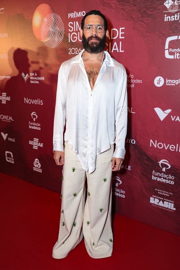 Drayson Menezzes optou por uma alfaiataria fluida e desconstruída em tons neutros. O ator veste um blazer oversized em tom areia sobre uma camisa de cetim marrom chocolate com gola pontuda aparente, criando um contraste elegante de texturas