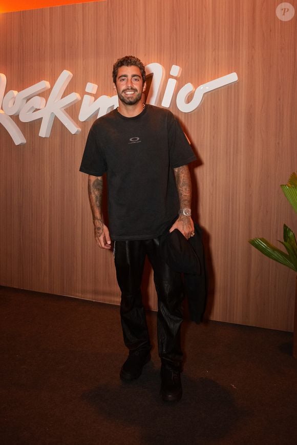 Pedro Scooby: o surfista investe na estética streetwear minimalista com uma camiseta preta oversized de malha encorpada e pequeno logotipo centralizado na altura do peito. Ele combina a peça com calça preta de couro de caimento reto, tênis pretos esportivos e relógio prateado de mostrador amplo, além de carregar uma jaqueta preta dobrada nas mãos