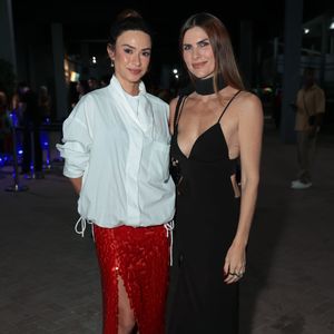 Thaila Ayala surgiu com um vestido preto minimalista de alças finas, decote profundo e recortes cut-out laterais, acompanhado de uma marcante gola choker preta e tênis escuros. Ela posou ao lado de uma acompanhante que vestia uma camisa oversized branca estruturada, saia vermelha texturizada com fenda frontal e tênis com estampa animal print. A dupla esbanjou ousadia e alta moda urbana