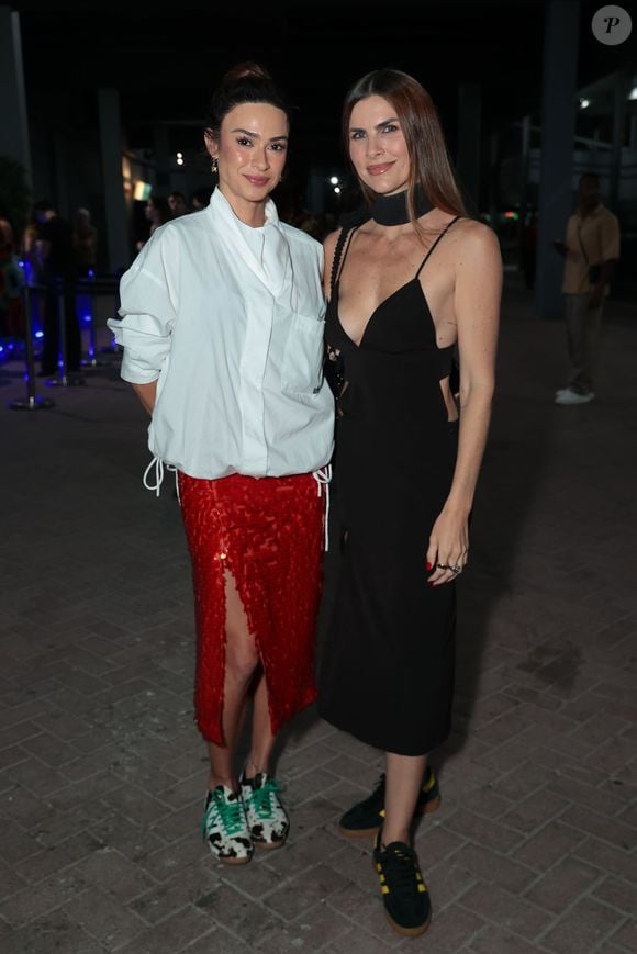 Thaila Ayala surgiu com um vestido preto minimalista de alças finas, decote profundo e recortes cut-out laterais, acompanhado de uma marcante gola choker preta e tênis escuros. Ela posou ao lado de uma acompanhante que vestia uma camisa oversized branca estruturada, saia vermelha texturizada com fenda frontal e tênis com estampa animal print. A dupla esbanjou ousadia e alta moda urbana
