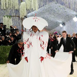 Naomi Osaka apostou na dramaticidade com um volumoso vestido branco de gola alta e ombreiras arquitetônicas, adornado com aplicações que remetem a pétalas vermelhas, finalizando com um chapéu monumental em formato de disco