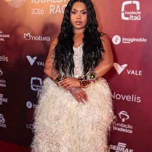 A cantora Duquesa brilhou em um vestido off-white que brinca com texturas volumosas e detalhes minuciosos. A peça apresenta um corpete em crochê ou renda delicada, que se transforma em uma saia ampla coberta por franjas longas e macias, criando um efeito de movimento impactante