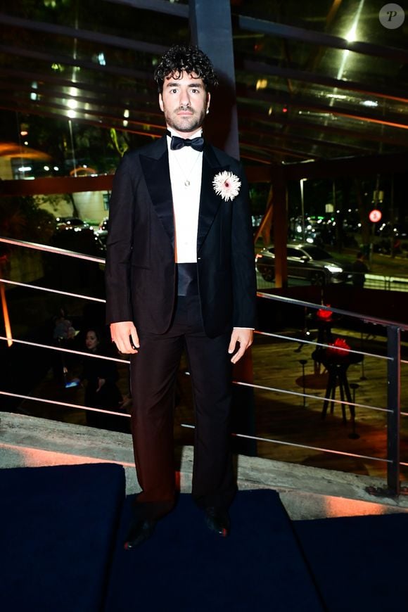 José Condessa: o ator português adotou um tuxedo clássico. O traje inclui um paletó preto com lapelas em cetim, calça de alfaiataria de corte reto com faixa na cintura (cummerbund) e camisa social branca com gravata-borboleta preta. O destaque do visual fica para o arranjo floral de flor branca aplicado na lapela