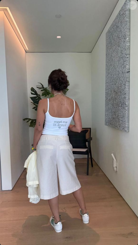 Em clima de Copa do Mundo, Anitta apostou em um visual casual e cheio de referências ao Brasil. A cantora surgiu com uma regata branca adornada por uma bandeira brasileira em strass, combinada com uma jorts em tom off-white e acessórios inspirados no futebol durante os ensaios para a aguardada cerimônia de abertura do Mundial de 2026