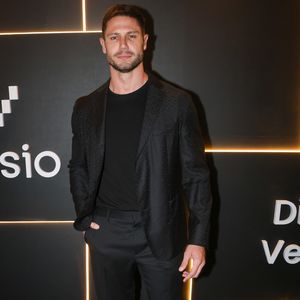 Jonas Sulzbach investe em um visual all black minimalista e contemporâneo, no melhor estilo esporte fino. Ele combina uma camiseta preta básica de gola careca com um blazer preto estruturado que possui uma sutil textura quadriculada ou jacquard no tecido, conferindo profundidade à peça. A calça de alfaiataria preta possui corte reto e caimento sob medida. Para quebrar a sobriedade monocromática e conferir um ar urbano e jovial à produção, Lucas finaliza o conjunto com tênis de couro totalmente brancos e de solado reto