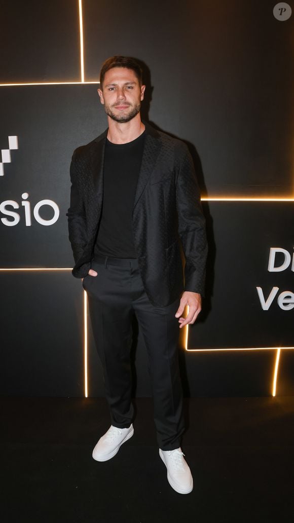 Jonas Sulzbach investe em um visual all black minimalista e contemporâneo, no melhor estilo esporte fino. Ele combina uma camiseta preta básica de gola careca com um blazer preto estruturado que possui uma sutil textura quadriculada ou jacquard no tecido, conferindo profundidade à peça. A calça de alfaiataria preta possui corte reto e caimento sob medida. Para quebrar a sobriedade monocromática e conferir um ar urbano e jovial à produção, Lucas finaliza o conjunto com tênis de couro totalmente brancos e de solado reto
