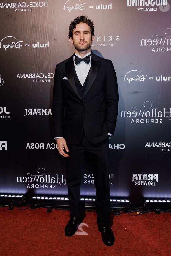 Felipe Ricca: o visual formal aposta em um tuxedo tradicional de três peças na cor preta, composto por paletó com lapela de cetim, colete ajustado e calça social de alfaiataria. A composição inclui camisa social branca com botões escuros, gravata borboleta preta, lenço de bolso branco dobrado e sapatos sociais pretos brilhantes