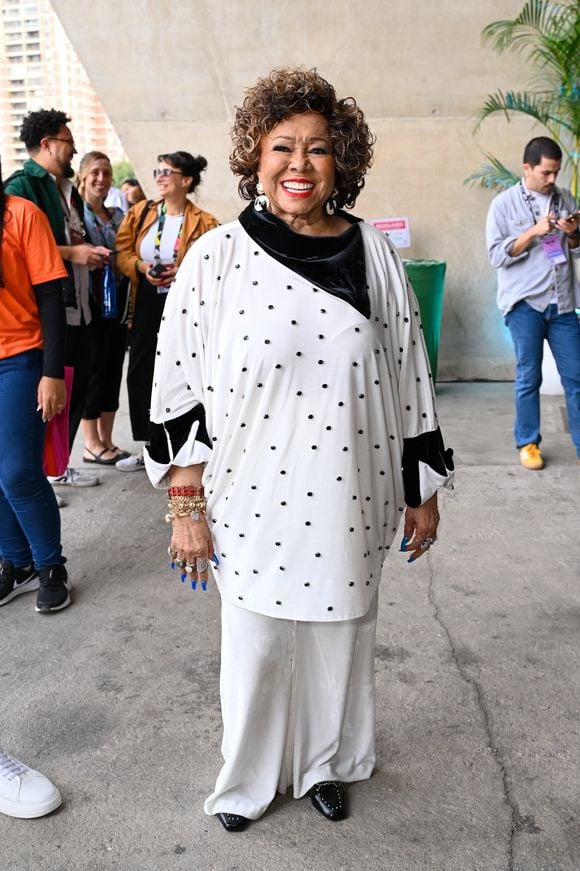 Alcione no Rio2C, a icônica Marrom mostra como transpor a sobriedade do corpcore para o seu DNA maximalista e sofisticado. Em vez da alfaiataria rígida tradicional, Alcione aposta em um conjunto fluido monocromático off-white, com uma reinterpretação tridimensional do clássico poá
