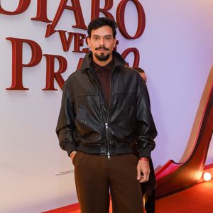 O ex-BBB Vinicius investiu em uma paleta de tons terrosos e texturas contrastantes. Ele veste uma jaqueta bomber de couro preto oversized com fechamento em zíper, sobreposta a uma camisa polo em tom de marrom café. A calça de alfaiataria possui corte reto e modelagem ampla (wide leg) em um tom de marrom médio