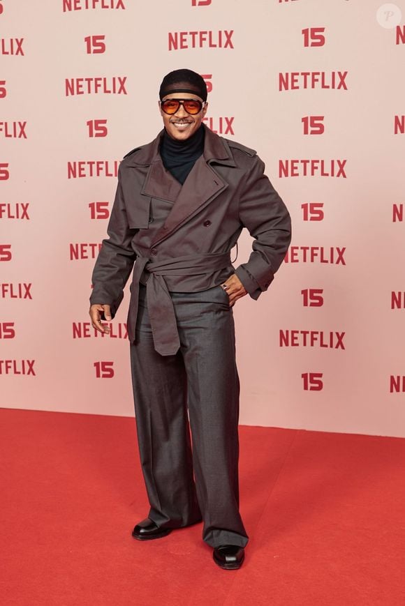 Humberto Moraes: veste um conjunto utilitário composto por jaqueta estilo trench coat curta transpassada com cinto amarado, blusa de gola alta escura, calça de alfaiataria cinza bem ampla, além de gorro e óculos de lentes alaranjadas
