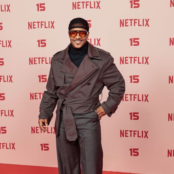 Humberto Moraes: veste um conjunto utilitário composto por jaqueta estilo trench coat curta transpassada com cinto amarado, blusa de gola alta escura, calça de alfaiataria cinza bem ampla, além de gorro e óculos de lentes alaranjadas