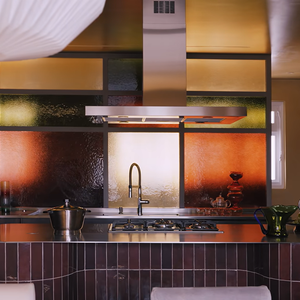 A cozinha é um dos destaques do dúplex de Manu Gavassi e Jullio Reis, com marcenaria planejada, bancadas de aço inoxidável, ilha revestida de porcelanato e um painel de vidros coloridos em tons de âmbar, verde e laranja. Segundo a Casa Vogue, é nesse ambiente que a cantora costuma preparar panquecas de banana para a filha, Nara