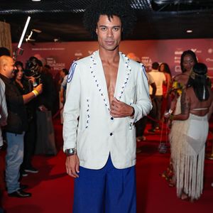 Breno Simões marcou presença com um visual que equilibra alfaiataria clássica e elementos náuticos. O ex-BBB veste um blazer off-white de linho, usado sem camisa, que se destaca pelos detalhes de búzios e cordões azuis aplicados na lapela e nos ombros