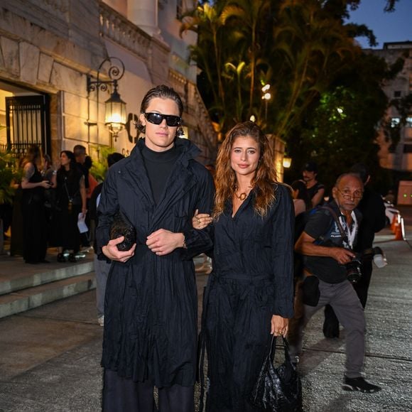 Isadora Cruz e Lucas Pinheiro: o casal surgiu em uma proposta dark academia fundida ao utilitarismo moderno, apostando no impacto visual das texturas monocromáticas. Isadora Cruz veste um macacão preto de tecido anasalado e aspecto 'amassado' proposital, com amarração na cintura e decote em "V", complementado por uma bolsa de ombro no mesmo material e um colar de elos dourados que ilumina o rosto