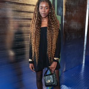 Liza Del Dala surgiu deslumbrante em uma proposta que valoriza o volume e o movimento, usando um vestido curto preto de decote ombro a ombro e mangas bufantes. O contraste entre o tecido fluido do vestido e a densidade das meias-calças pretas criou uma base sólida para os acessórios de peso: braceletes dourados largos e um par de slingbacks de bico fino