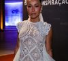 O modelo, com construção elaborada e camadas em movimento, traz ainda uma gola marcante e cauda sutil, transformando o artesanal em peça de alta moda. Nos pés, o scarpin branco arremata a proposta monocromática, enquanto o beauty look polido adiciona ainda mais força à composição
