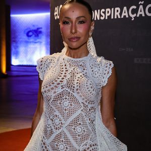 O modelo, com construção elaborada e camadas em movimento, traz ainda uma gola marcante e cauda sutil, transformando o artesanal em peça de alta moda. Nos pés, o scarpin branco arremata a proposta monocromática, enquanto o beauty look polido adiciona ainda mais força à composição