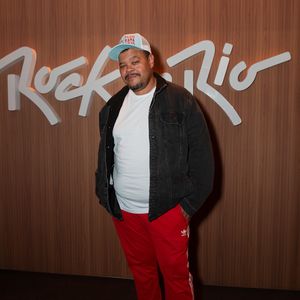 Babu Santana investe em uma proposta streetwear urbana e esportiva. O ator e cantor combina uma camiseta branca básica sobreposta por uma jaqueta jeans escura aberta e calça de agasalho vermelha com listras laterais brancas, arrematando a produção com tênis brancos e boné de aba curva com detalhe azul e estampa frontal