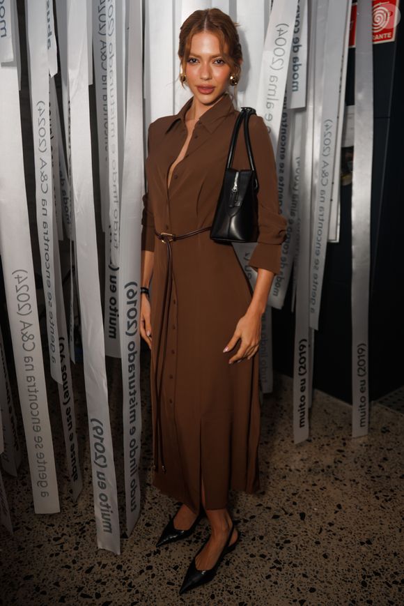 Jordanna Maia compareceu ao evento vestindo um vestido chemise midi marrom de botões frontais e fendas laterais discretas. O look foi acinturado por um cinto fino da mesma cor e finalizado com scarpins pretos de bico fino e modelo slingback. Ela também usava uma bolsa de ombro preta estruturada