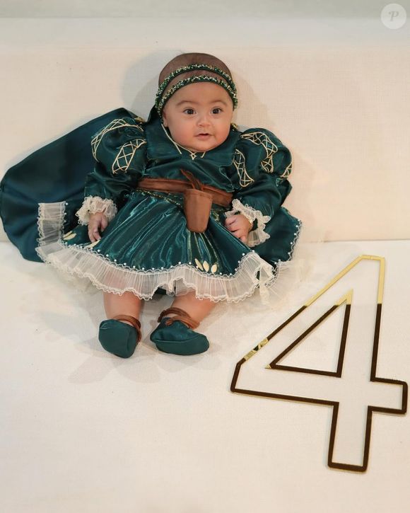 A pequena posa ao lado do número 4, celebrando seu quarto mês de vida