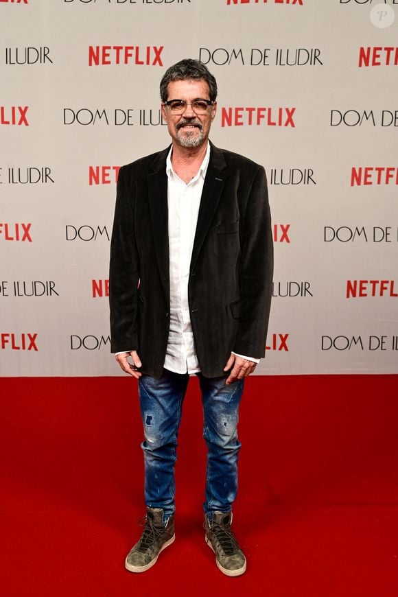 Felipe Camargo aposta em um visual despojado, combinando um blazer de veludo cotelê marrom escuro com uma camisa de botão branca de linho. Ele usa calças jeans azuis claras com efeito estonado e detalhes puídos, finalizando com tênis casuais de cano alto em lona verde oliva e solado branco