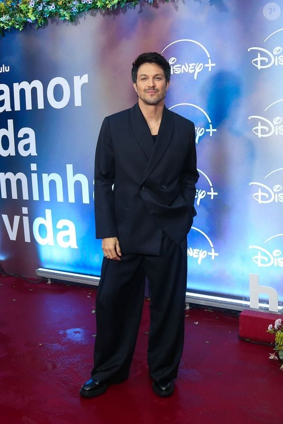 Rômulo Estrela: apresenta uma proposta moderna de alfaiataria em um terno risca-de-giz azul-marinho de modelagem oversized, com paletó transpassado de caimento solto e calça pantalona ampla, completando a produção com sapatos pretos de sola tratorada