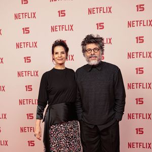 Helena Rinaldi e Daniel Alvim: Helena veste blusa preta de mangas três quartos combinada a uma saia longa estampada de padronagem floral/mosaico com faixa drapeada na cintura; Daniel acompanha o tom sóbrio usando blusa de tricot cinza-escuro sobre camisa de gola, calça preta ampla e tênis escuro de sola branca