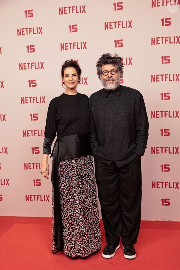 Helena Rinaldi e Daniel Alvim: Helena veste blusa preta de mangas três quartos combinada a uma saia longa estampada de padronagem floral/mosaico com faixa drapeada na cintura; Daniel acompanha o tom sóbrio usando blusa de tricot cinza-escuro sobre camisa de gola, calça preta ampla e tênis escuro de sola branca