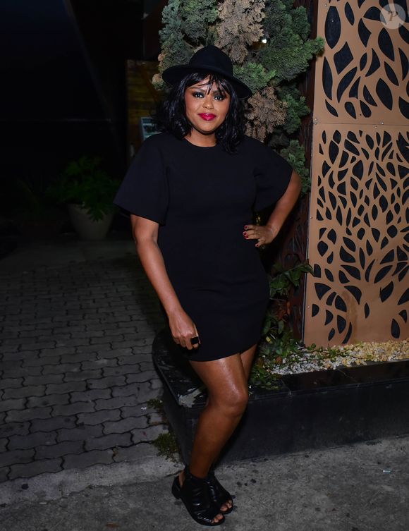 Carla Cristina Cardoso em um visual totalmente preto com forte apelo elegante e urbano. Ela usa um vestido curto de modelagem reta, com mangas amplas que conferem estrutura ao visual. Nos pés, sandálias pretas de salto com abertura frontal, reforçando a estética moderna