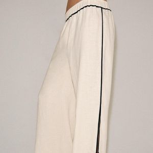 A calça de linho surge como uma das apostas para a Primavera 2026, com modelagem ampla, cintura média, cós elástico e fendas laterais que deixam a peça mais fresca para os dias de calor no Brasil. O detalhe de debrum em contraste acrescenta um toque sofisticado ao visual. Na Zara, custa R$ 439
