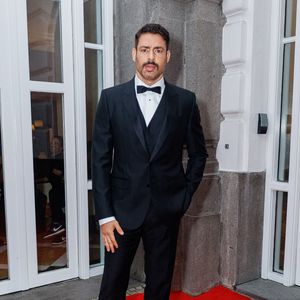 Cauã Reymond exibe um traje de gala clássico e rigoroso, composto por um smoking de três peças na cor preta. O conjunto inclui paletó de lapela fina, colete ajustado e calças de alfaiataria coordenadas