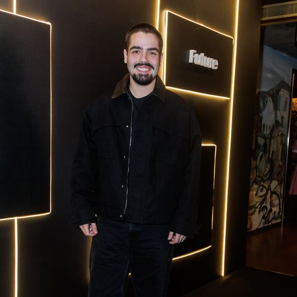 Filho de Faustão, João Guilherme Silva aposta em uma estética urbana e minimalista com uma proposta inteiramente voltada para tons escuros. Ele veste uma jaqueta de sarja preta estruturada, de modelagem ampla estilo oversized, caracterizada por lapelas proeminentes e fechamento em zíper frontal. Por baixo, complementa com uma camiseta básica preta de gola careca. A parte inferior é composta por uma calça jeans preta de corte reto e lavagem discreta