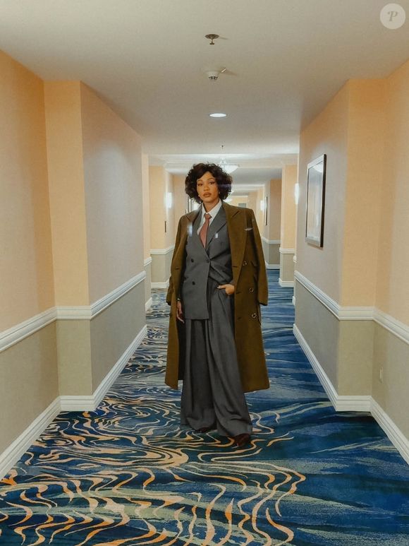 Luedji caminhou pelos corredores do hotel como se fosse parte de um filme. O terno cinza oversized, de ombreiras destacadas, ganha movimento com a calça amplíssima e um sobretudo verde-oliva que parece ter saído de um filme noir contemporâneo. A gravata rosada adiciona charme irônico, enquanto o cabelo volumoso completa um visual autoral, cheio de presença e dramaticidade fashion. Um look que une arte, irreverência e elegância, como tudo que Luedji faz