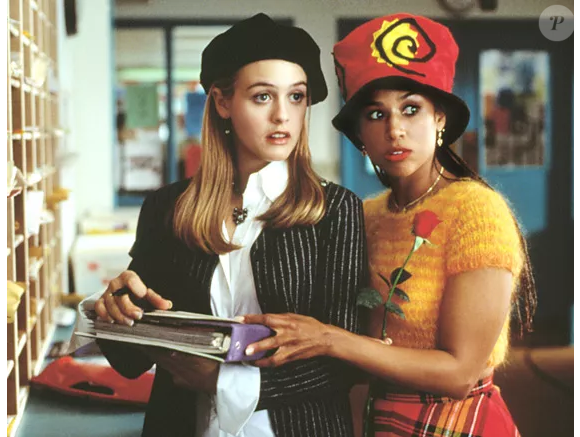 Com boina estilosa, jaqueta listrada e camisa impecável, Cher assume ares profissionais ao tentar juntar seus professores, Sr. Hall e Srta. Geist.