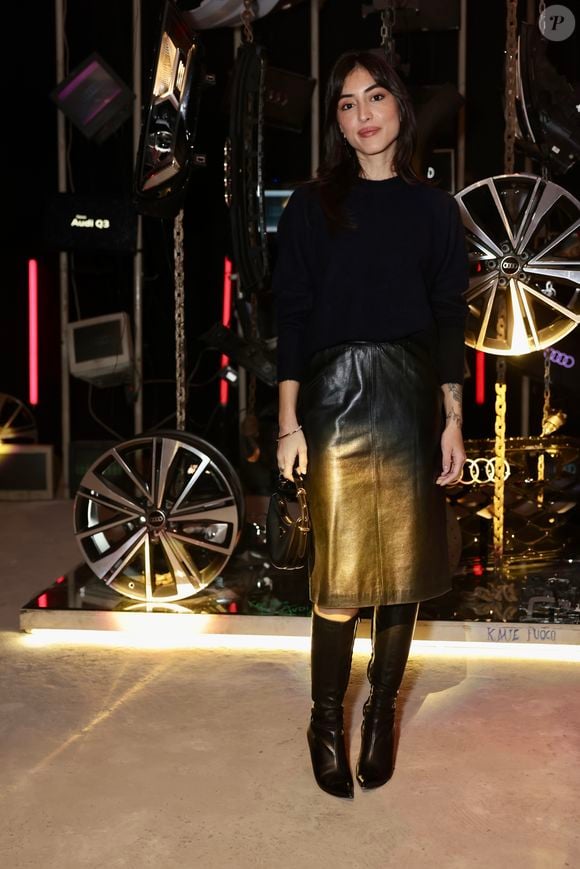 Maju Trindade ostenta um visual sofisticado e moderno com foco em contrastes de luz. Na parte superior, ela utiliza uma blusa de tricô preta de mangas longas, gola alta discreta e caimento ajustado ao corpo. O grande destaque da produção é a saia de couro de comprimento mídi com efeito ombré, que transita gradualmente do preto na cintura para um dourado metalizado envelhecido em direção à barra, criando um reflexo luminoso