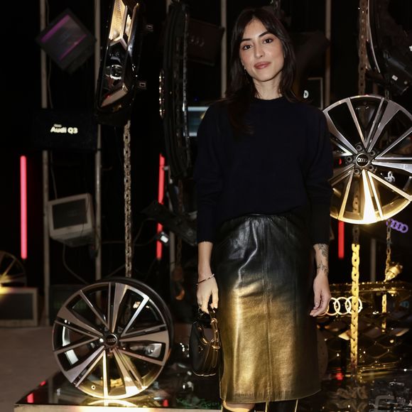 Maju Trindade ostenta um visual sofisticado e moderno com foco em contrastes de luz. Na parte superior, ela utiliza uma blusa de tricô preta de mangas longas, gola alta discreta e caimento ajustado ao corpo. O grande destaque da produção é a saia de couro de comprimento mídi com efeito ombré, que transita gradualmente do preto na cintura para um dourado metalizado envelhecido em direção à barra, criando um reflexo luminoso