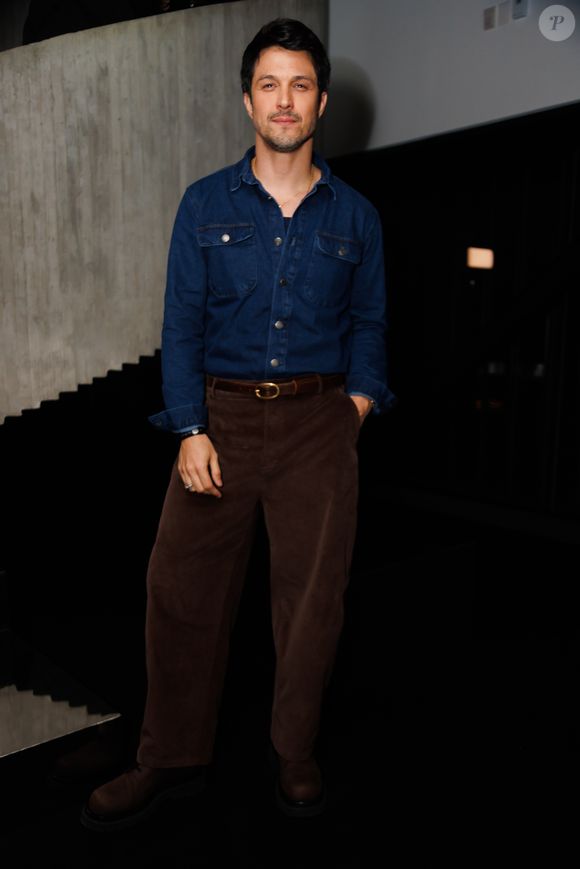 Romulo Estrela apostou em um visual casual elegante com camisa jeans de lavagem escura e botões frontais abertos, combinada a uma calça de veludo cotelê marrom-escuro de modelagem reta. O look é ajustado por um cinto de couro com fivela oval dourada e finalizado com sapatos escuros de sola tratorada