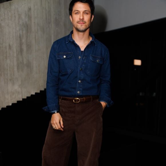 Romulo Estrela apostou em um visual casual elegante com camisa jeans de lavagem escura e botões frontais abertos, combinada a uma calça de veludo cotelê marrom-escuro de modelagem reta. O look é ajustado por um cinto de couro com fivela oval dourada e finalizado com sapatos escuros de sola tratorada