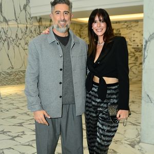 Suzana Gullo apostou na tendência glow com uma calça de alfaiataria em listras horizontais brilhantes texturizadas, combinada a um top cropped preto transpassado com amarração frontal e blazer clássico estruturado. O visual clean de Marcos Mion contrastou com a produção da esposa, trazendo um conjunto monocromático cinza composto por calça oversized, suéter de gola V e jaqueta de botões, arrematado por tênis casuais estampados