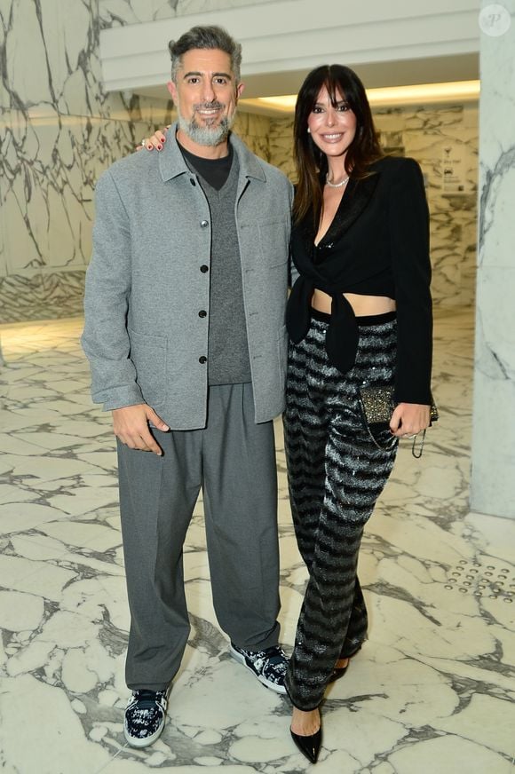Suzana Gullo apostou na tendência glow com uma calça de alfaiataria em listras horizontais brilhantes texturizadas, combinada a um top cropped preto transpassado com amarração frontal e blazer clássico estruturado. O visual clean de Marcos Mion contrastou com a produção da esposa, trazendo um conjunto monocromático cinza composto por calça oversized, suéter de gola V e jaqueta de botões, arrematado por tênis casuais estampados