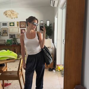 A atriz surge com regata branca ajustada, peça curinga que valoriza a silhueta sem esforço, combinada à calça preta de modelagem ampla, com barra dobrada, trazendo um ar relaxado e atual. É aquele visual que é  “despretensiosamente elegante”, como define o próprio street style contemporâneo