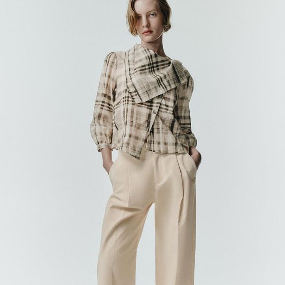 Entre os destaques da coleção da Zara está a Camisa Xadrez Lenço, uma peça cinza com gola tipo lenço, mangas abaixo do cotovelo e fechamento frontal cruzado com botões