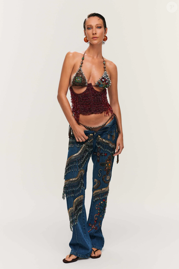 A produção aposta em calça jeans de lavagem escura, de modelagem reta, com bordados ondulares em tons de dourado, vermelho e cobre, que acrescentam personalidade e sofisticação ao visual.